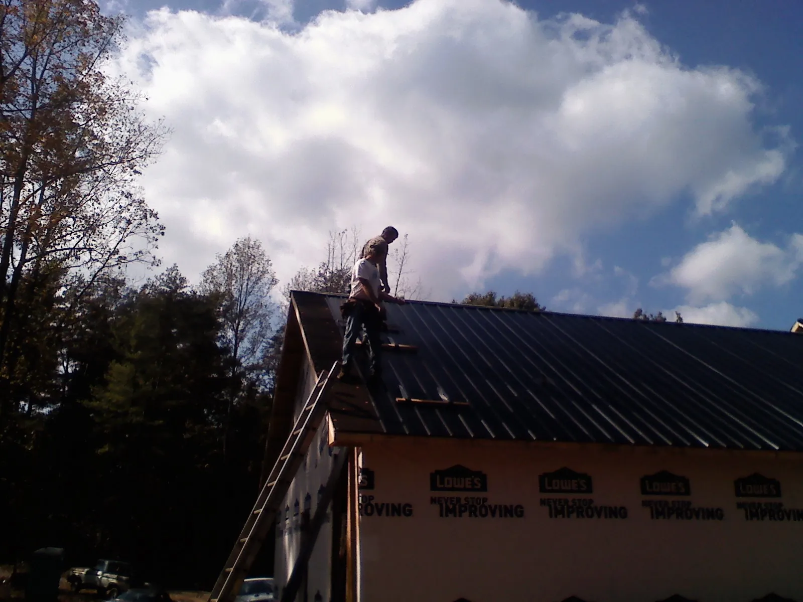 Roofer fastening dark metal panels high against a cloudy sky, from a Roof Inspection job in Courtland